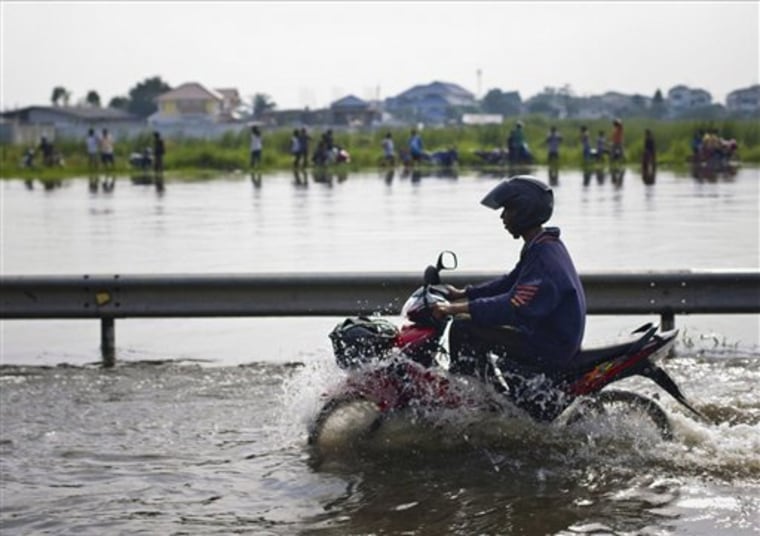 A motorcyclist rides through a flooded road beside an overflowing canal as residents catch fish on the other side on the outskirts of Bangkok, Thailand Thursday.